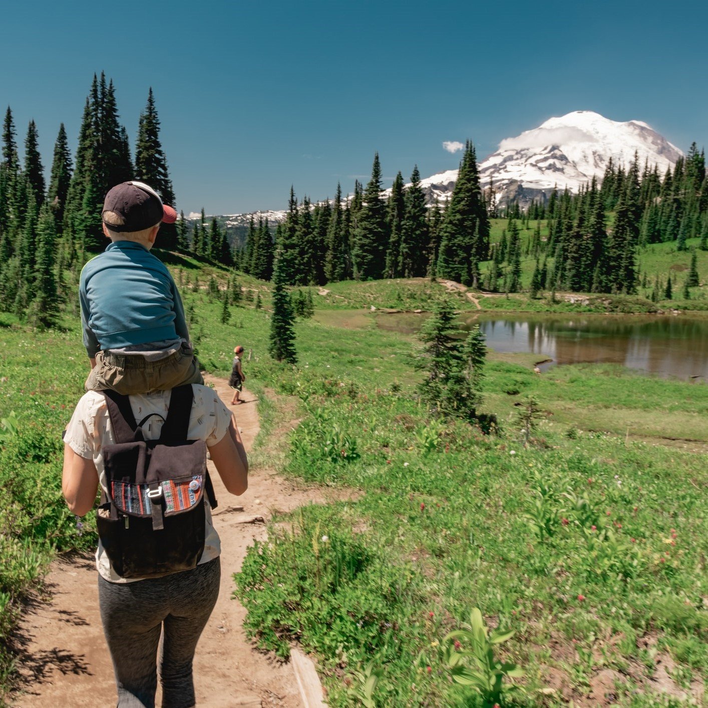 A woman carries a child on her back as she hikes toward Mount Rainier in Washington.